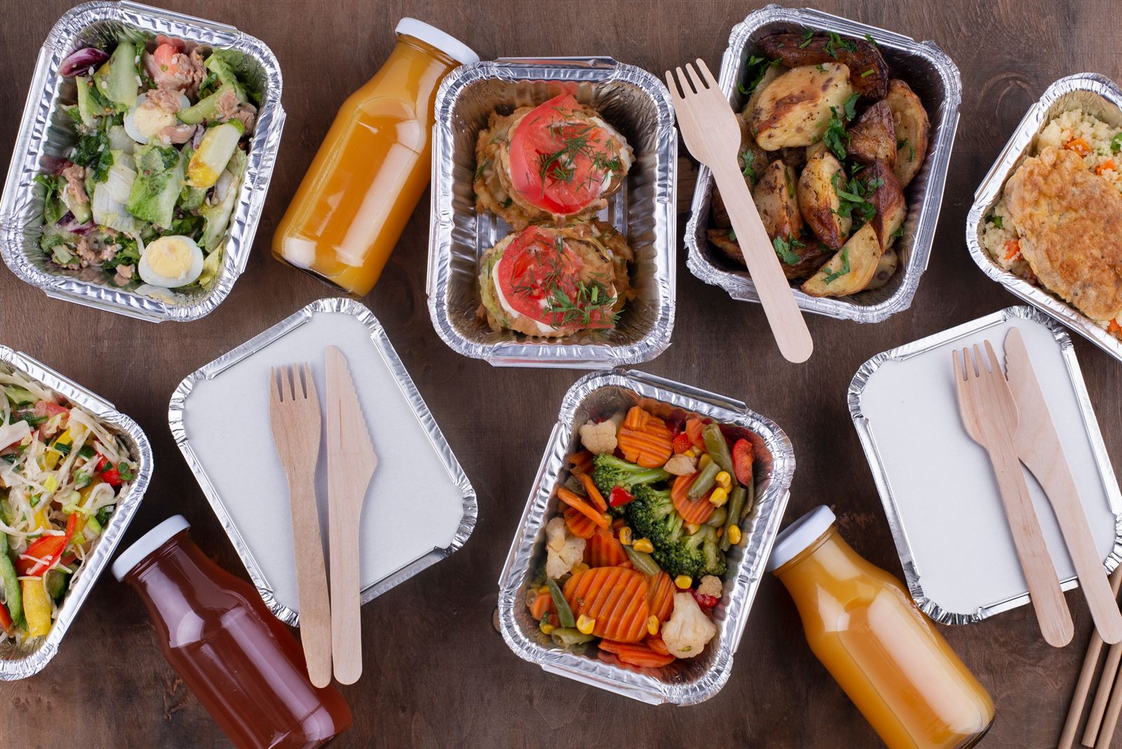Prepared meals, salads, roasted vegetables, and fresh juices arranged on a dark wooden table.